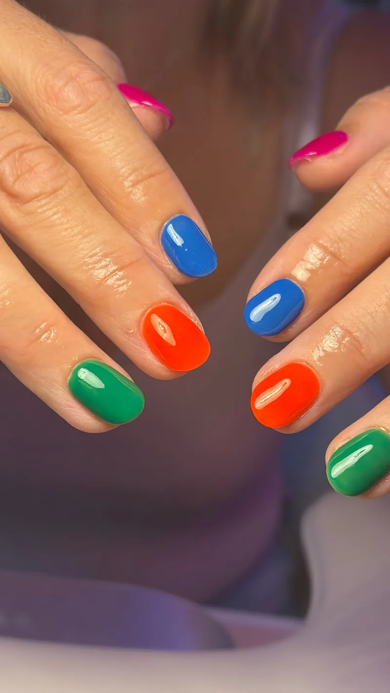 Glossy nails in pink, blue, orange and green, a different colour on each finger, by Rosie Mae Beauty